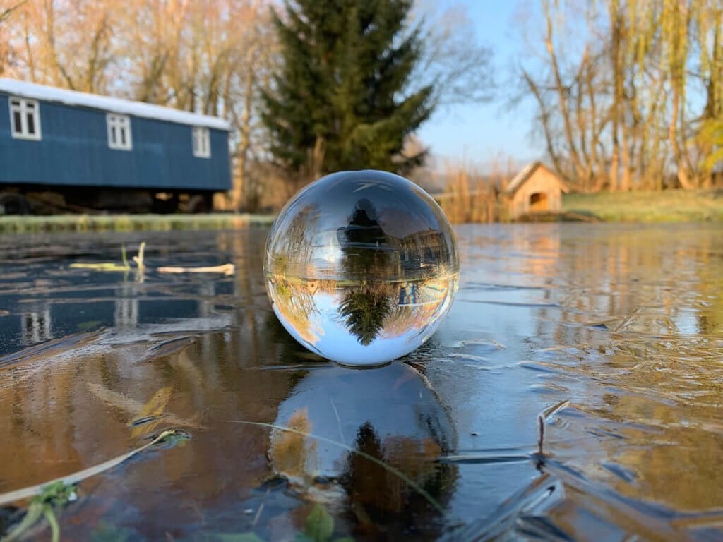 Lensball auf gefrorenem Teich – sieht nicht nur schön aus, sondern ist auch lustig: Wenn man die Kugel dreht, hört sie nicht mehr auf, sich zu drehen, weil die Reibung zwischen Eis und Glas so gering ist.